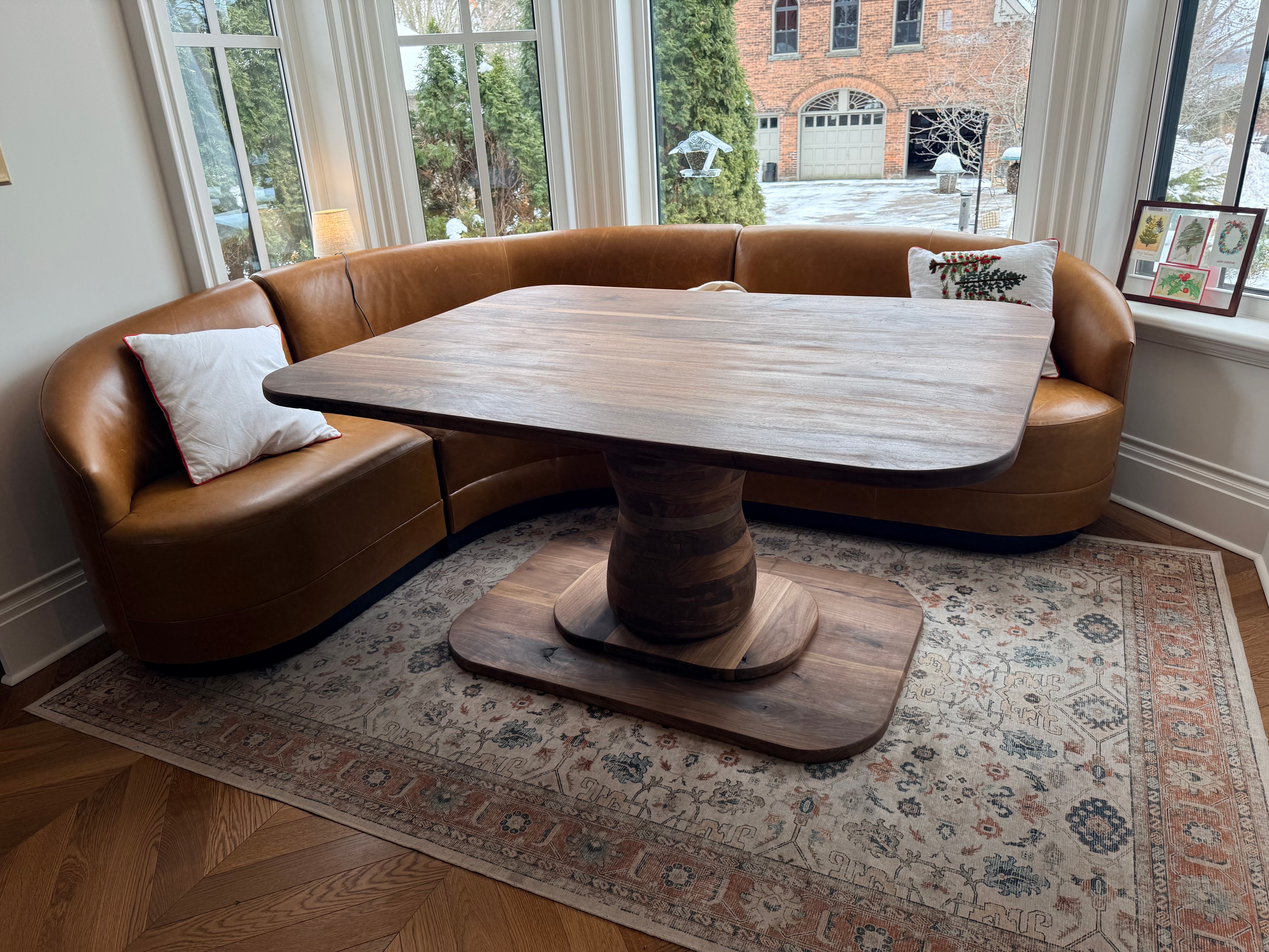 Custom walnut pedestal dining table with curved leather banquette